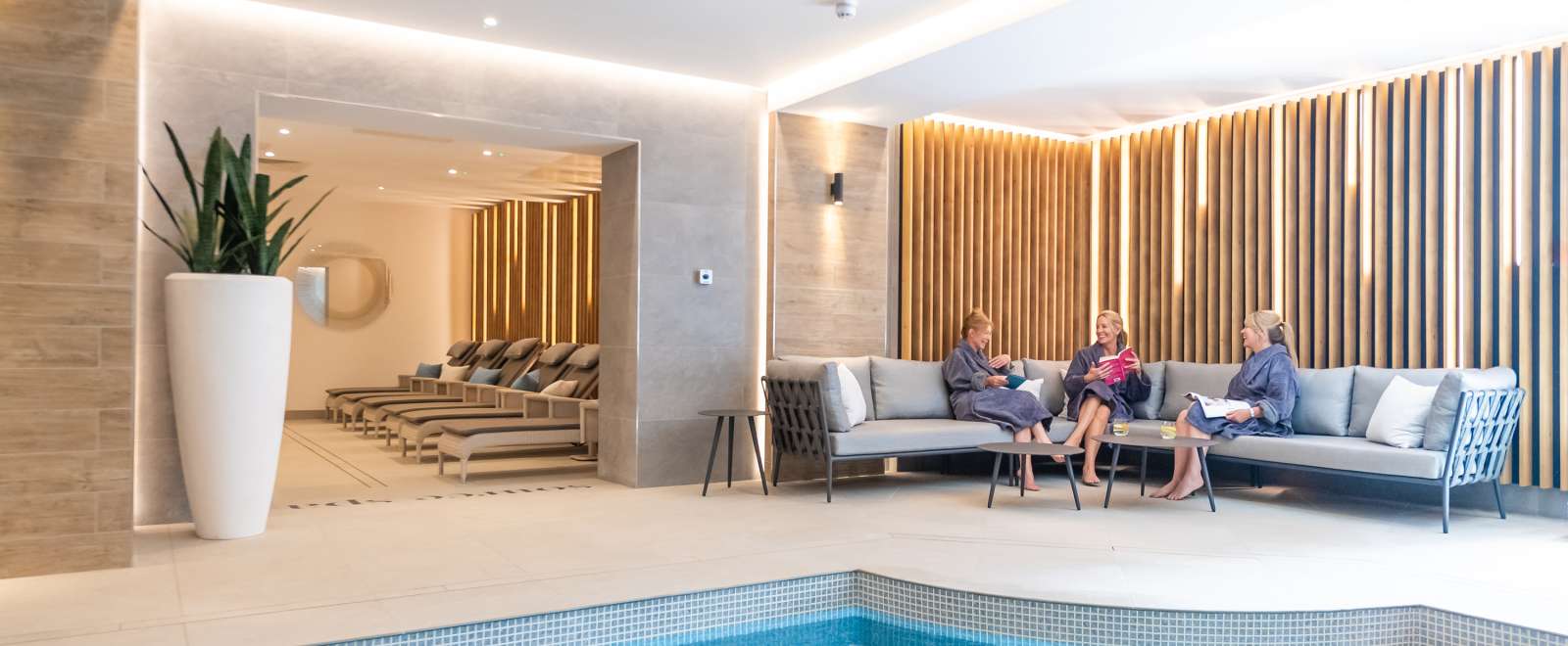 Three ladies sat on sofa near indoor pool 